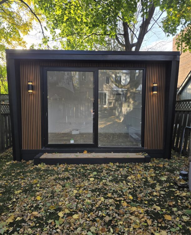 Modern custom-built garden room in a backyard, featuring large glass windows and a cozy interior setup for work or relaxation.