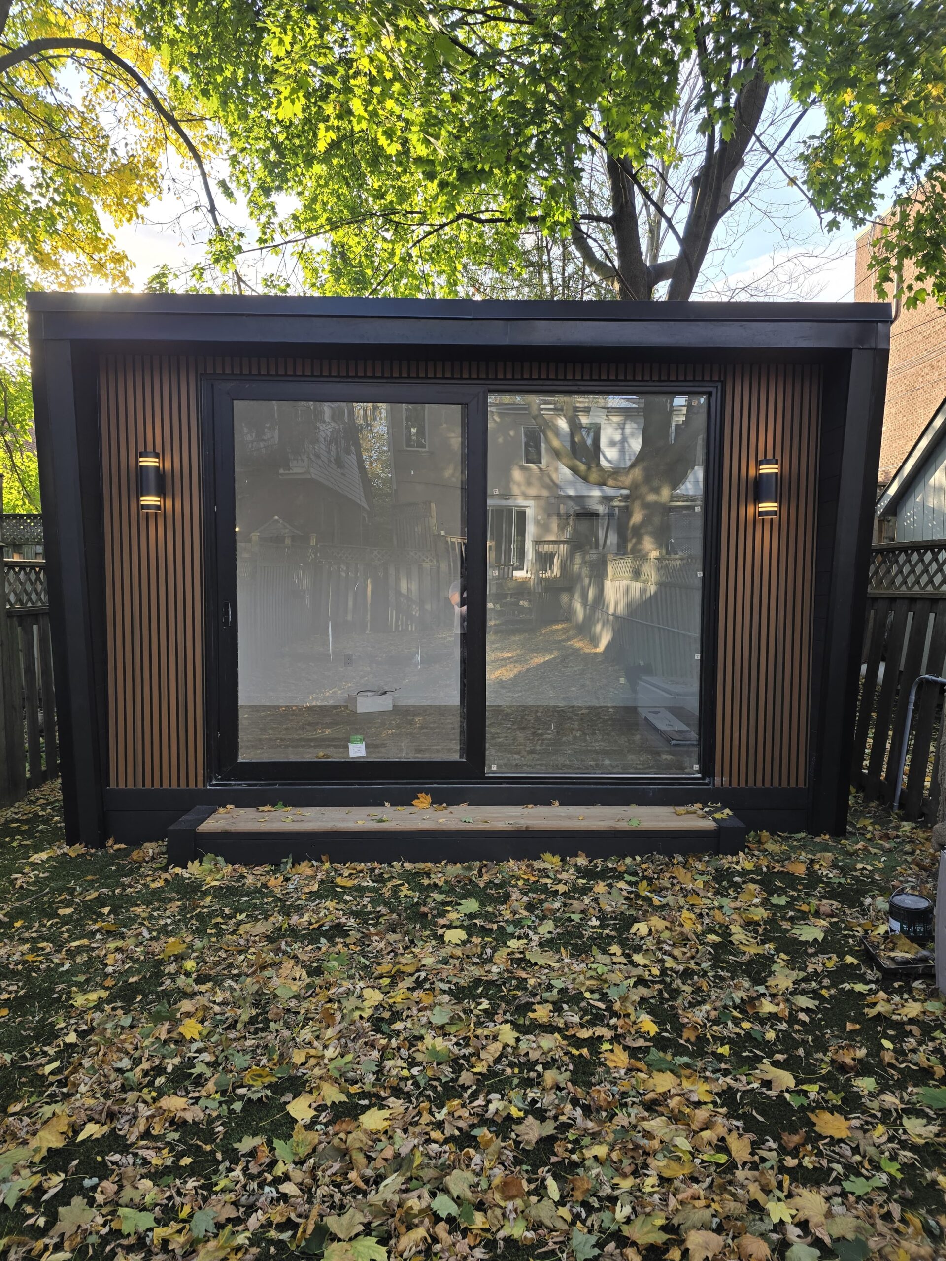 Modern custom-built garden room in a backyard, featuring large glass windows and a cozy interior setup for work or relaxation.