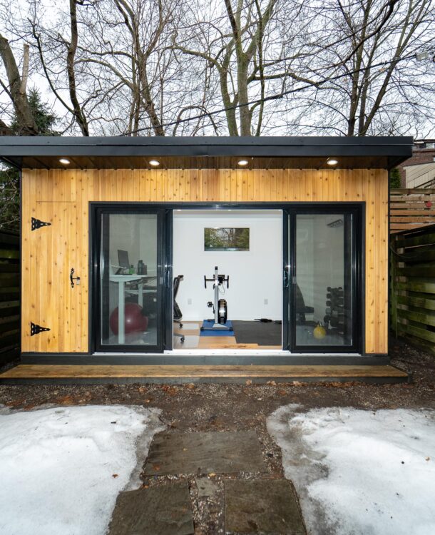 Modern custom-built garden room in a backyard, featuring large glass windows and a cozy interior setup for work or relaxation