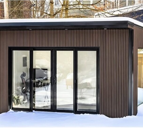 Garden room converted into a home office with a desk, plants, and natural light streaming through large windows