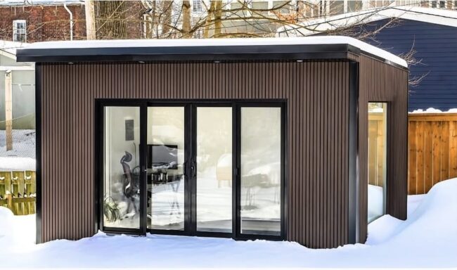 Garden room converted into a home office with a desk, plants, and natural light streaming through large windows