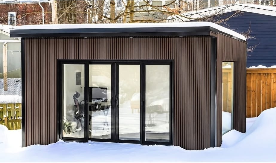 Garden room converted into a home office with a desk, plants, and natural light streaming through large windows