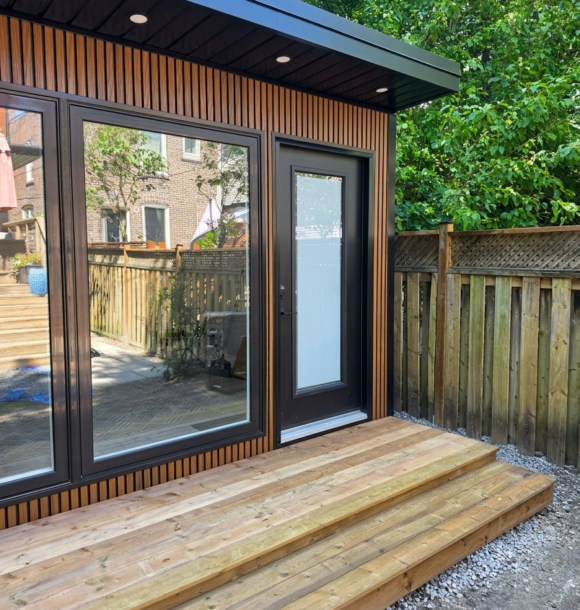 Modern custom garden office with black-framed windows, glass door, wood-look exterior and deck in a Toronto backyard